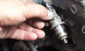 Main d'un mécanicien tenant un injecteur diesel sale. Le prix de la réparation d'injecteur diesel peut varier.