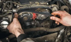Mains ajustant la courroie de distribution d'un moteur. Le temps pour changer une courroie de distribution varie selon le modèle de voiture.