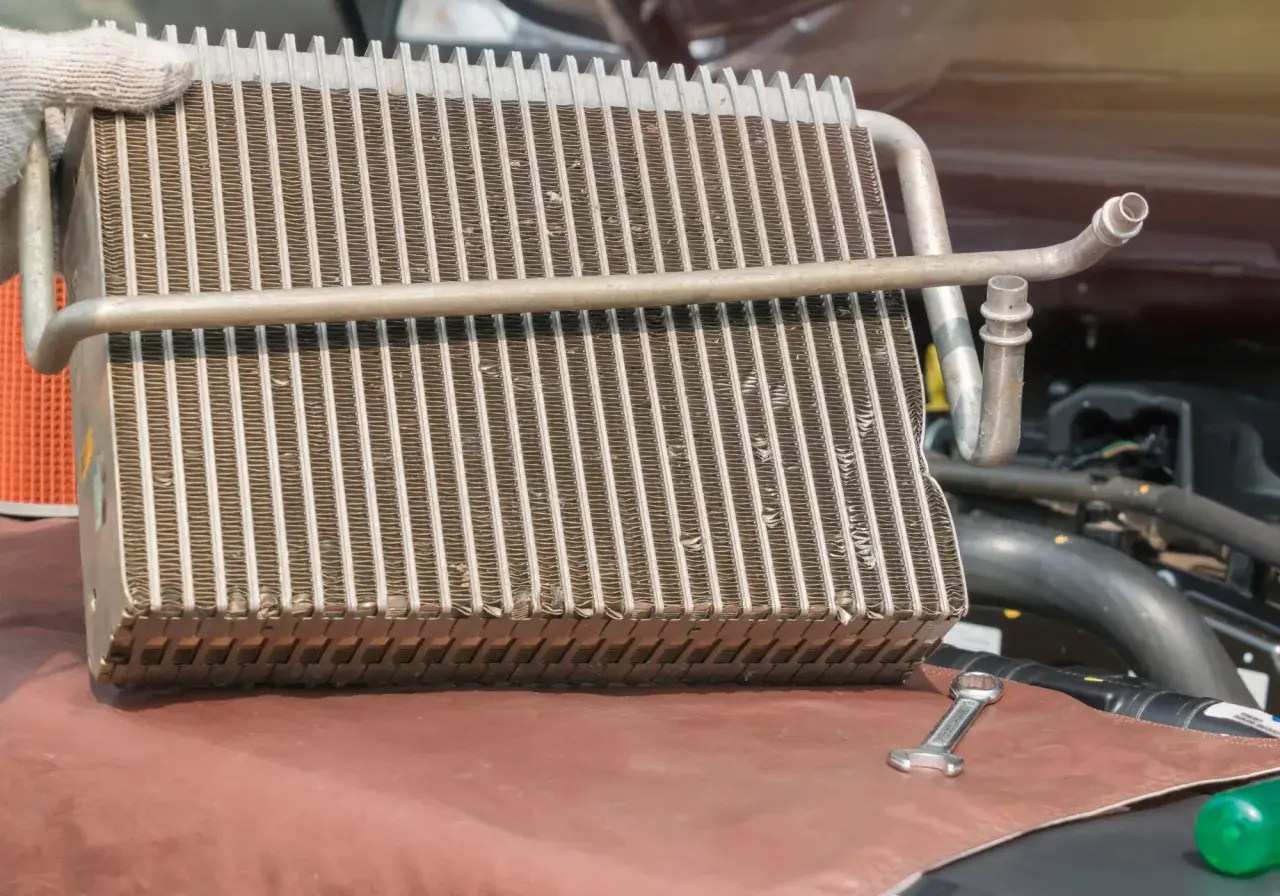 Main d'un mécanicien tenant un radiateur de voiture pour sa réparation. Une clé est posée à côté.