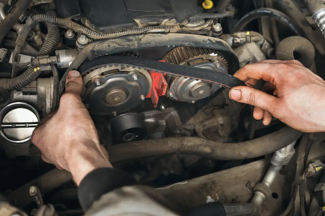 Mains ajustant la courroie de distribution d'un moteur. Le temps pour changer une courroie de distribution varie selon le modèle de voiture.
