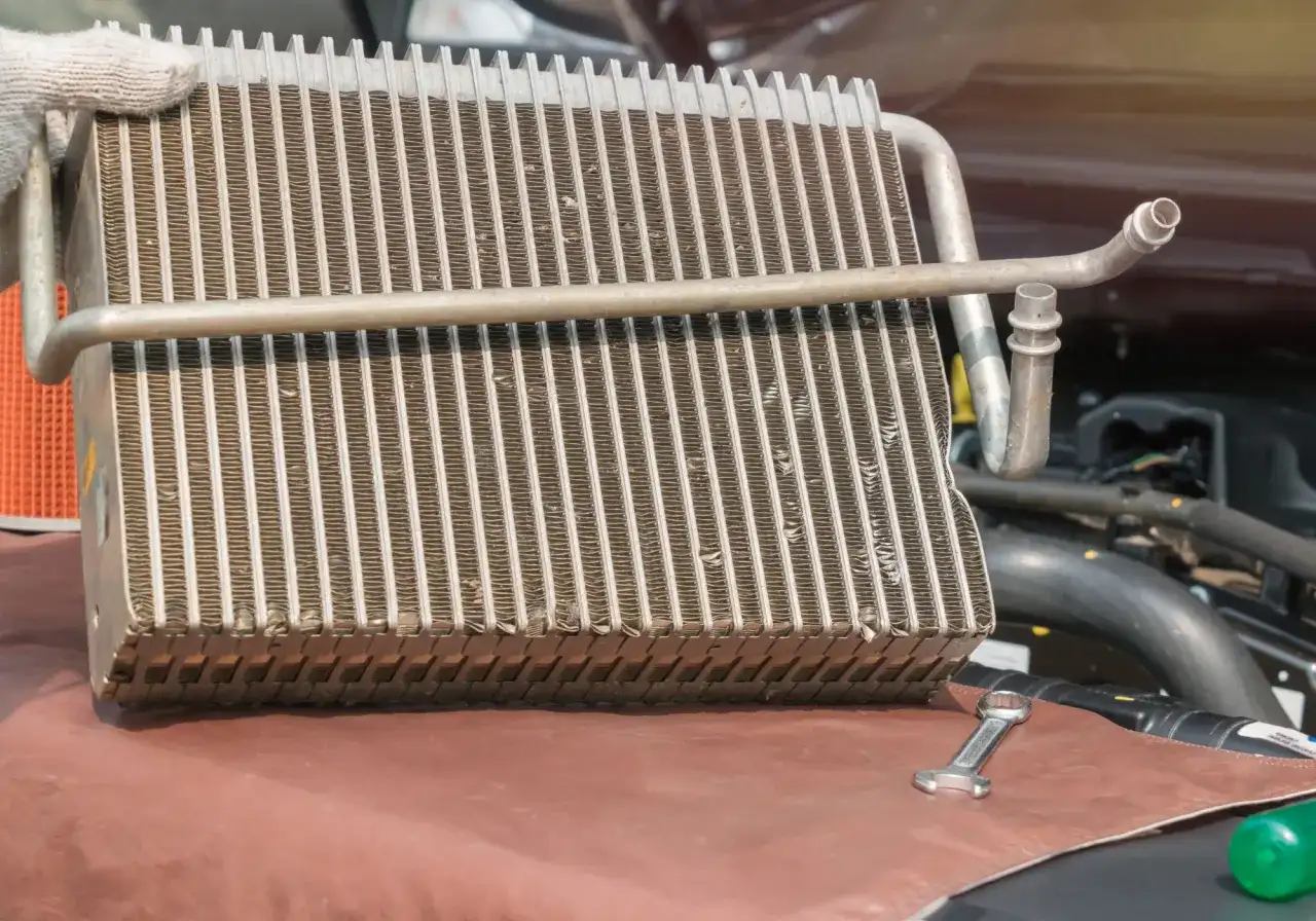 Main d'un mécanicien tenant un radiateur de voiture pour sa réparation. Une clé est posée à côté.