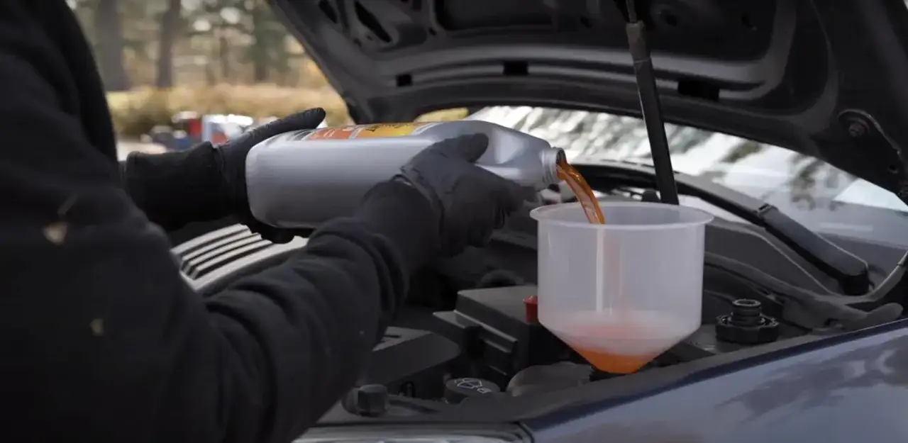 Maintenant, découvrez comment purger le liquide de refroidissement sans vis de purge. On verse le liquide orange dans un entonnoir.
