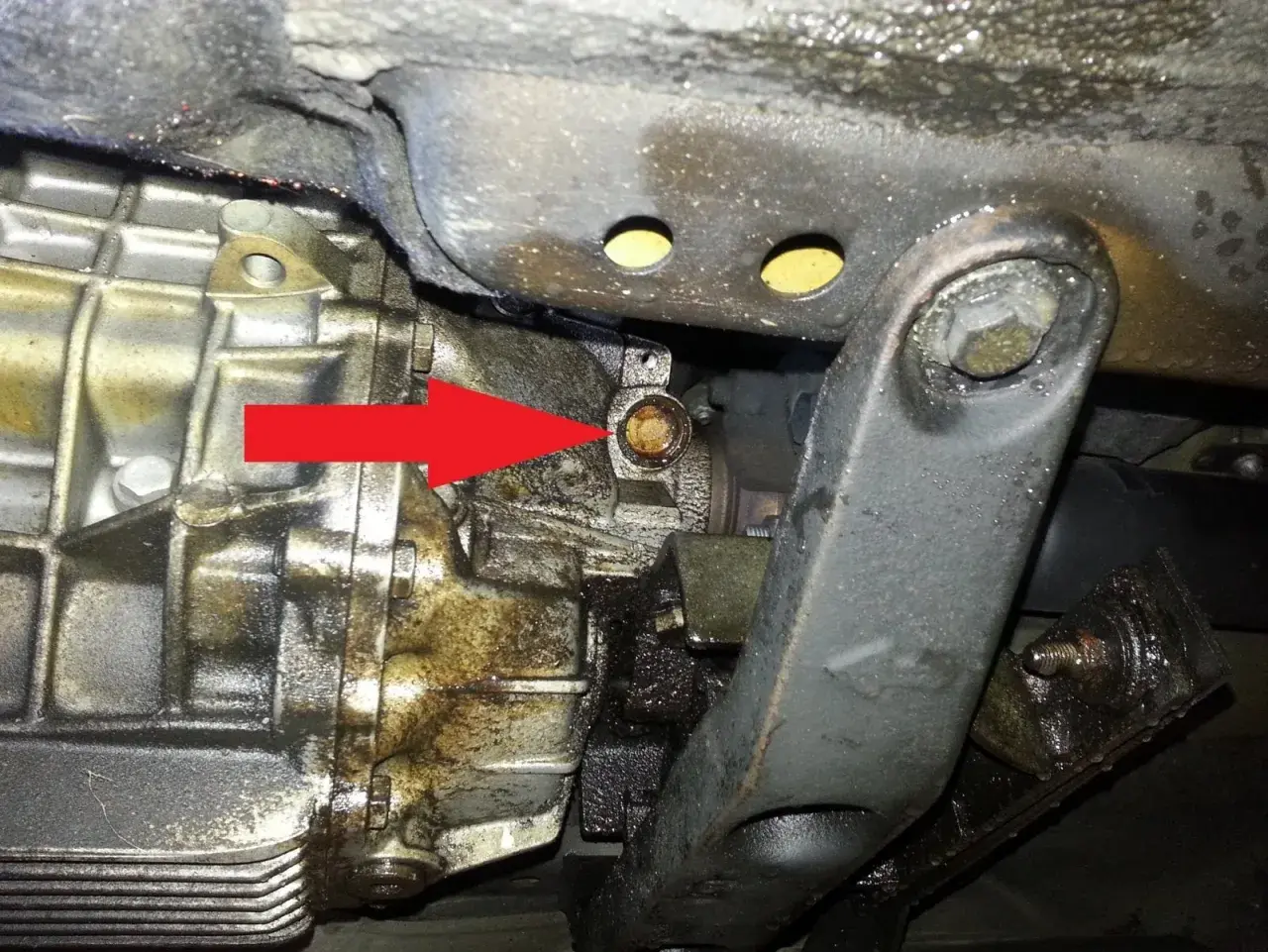Flèche rouge pointant vers une tache d'huile, signe d'une fuite d'huile de boîte de vitesse sur un véhicule.