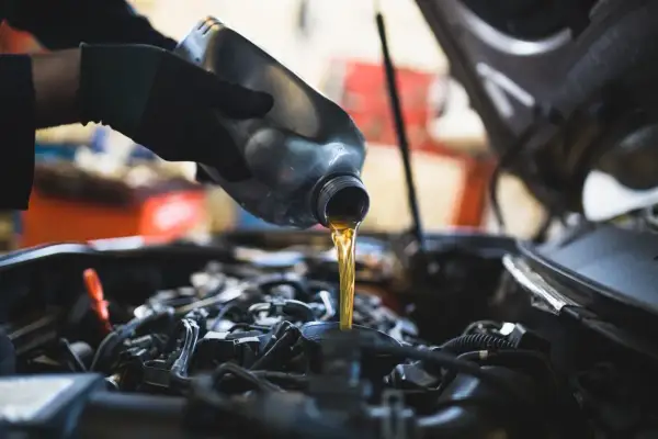 Main d'un mécanicien versant de l'huile neuve dans le moteur d'une Dacia Sandero lors d'une vidange.