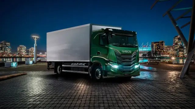 Modèle camion vert Iveco, prêt pour une livraison nocturne dans une ville illuminée.