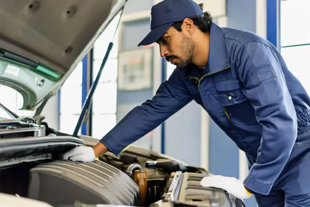 Mécanicien en bleu, casquette, gants blancs, travaillant sur le moteur. Il s'occupe de nettoyer injecteur qui claque pour une meilleure performance.