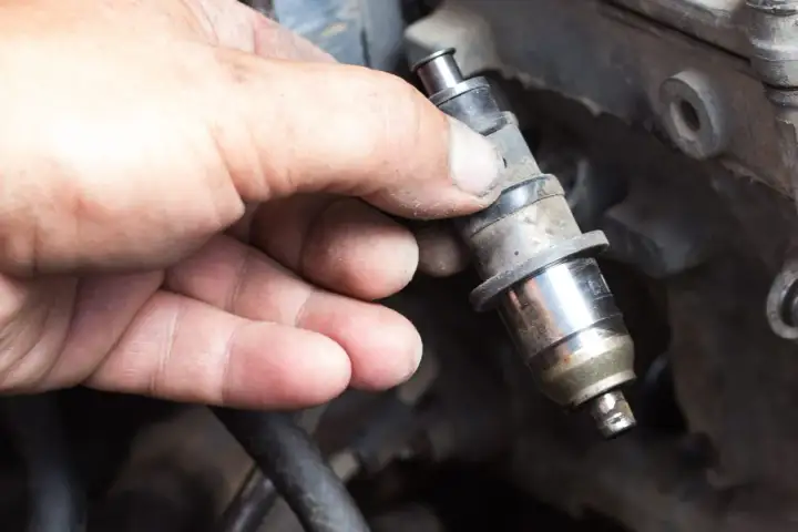 Main d'un mécanicien tenant un injecteur diesel sale. Le prix de la réparation d'injecteur diesel peut varier.